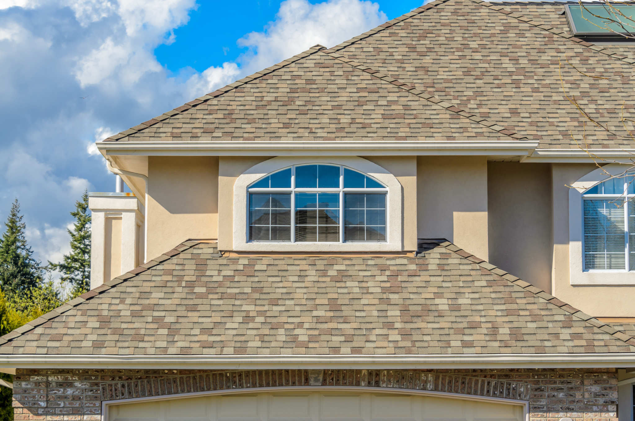 Upper part of a house with a textured roof, beige walls, and two windows under a clear sky